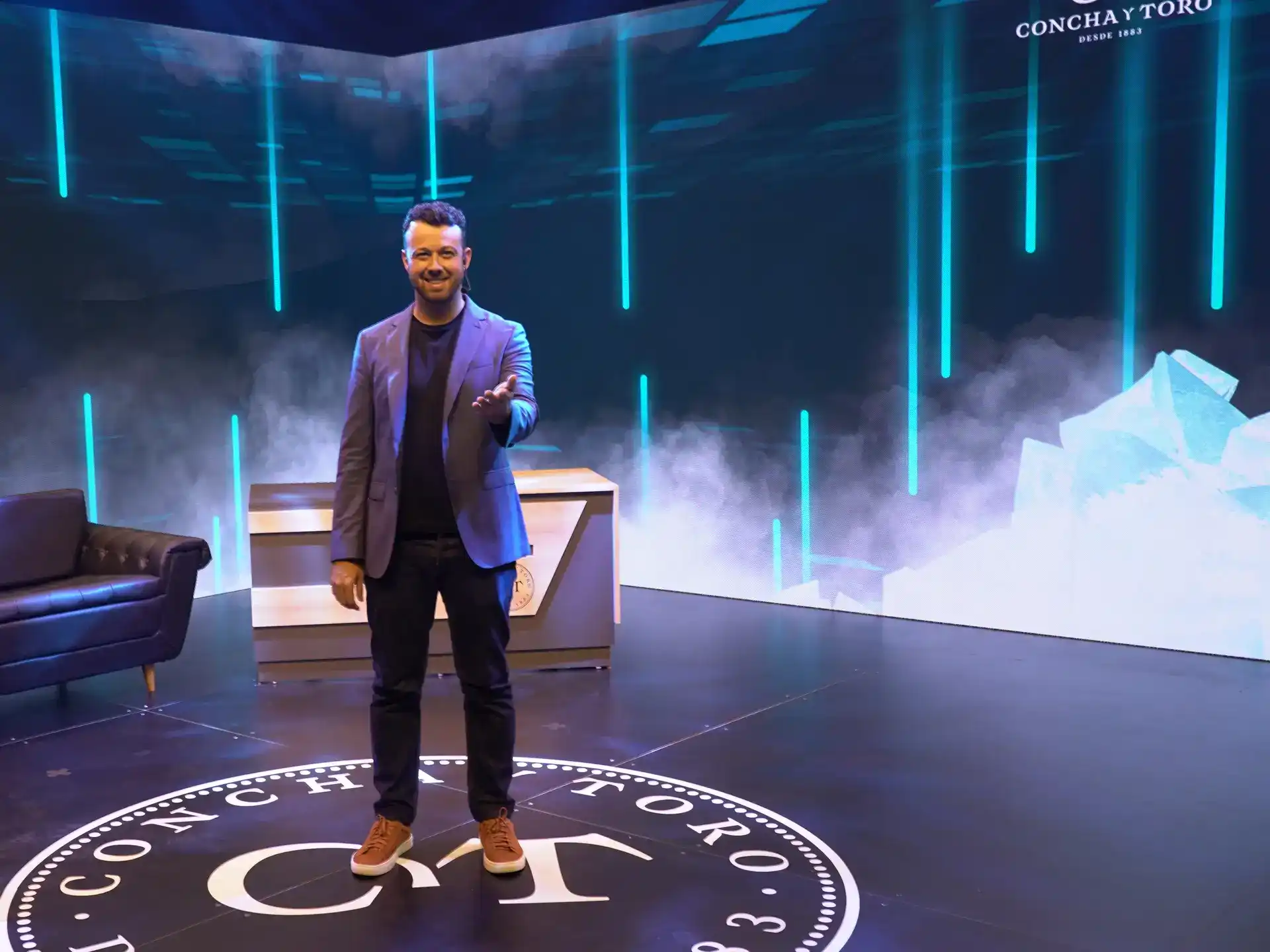 Tiago Lopes no palco apresentando um evento corporativo, em cenário com telão e iluminação azul