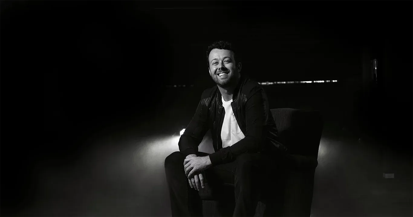 Tiago Lopes, palestrante corporativo, sorrindo sentado em uma poltrona