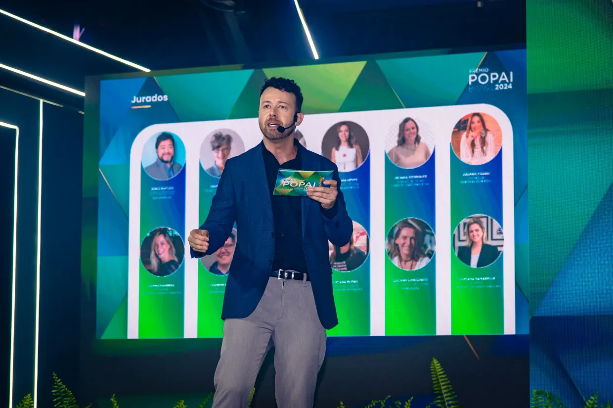 Tiago Lopes apresentando evento corporativo em palco com telão